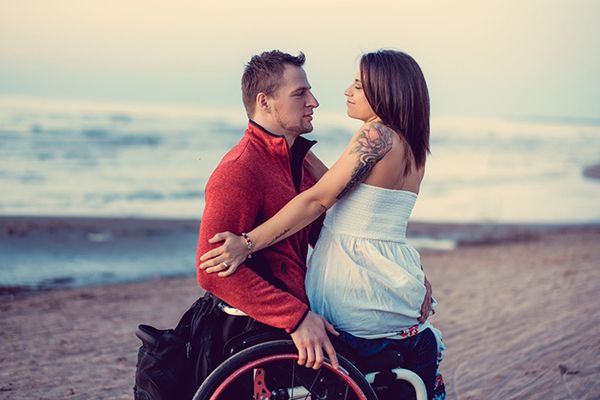 Homme en chaise roulante avec une femme assise sur ses genoux.